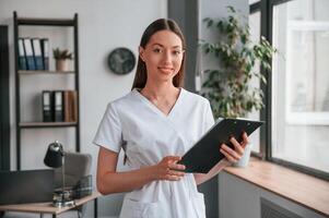 Smiling young beautiful ,woman in white clothes is in the office with notepad. photo