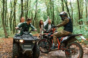 Two couples, on ATV with man that is on the bike in the forest that looking at the camera photo