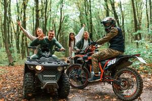 Two couples ,on ATV with man that is on the bike in the forest that looking at the camera photo
