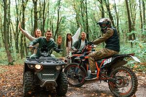 Two, couples ,on ATV with man that is on the bike in the forest that looking at the camera photo