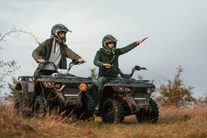 Showing the path by a hand. Two men are on the quad bikes outdoors on the field photo