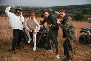 Two couples is with, quad bikes on the field. Men are having fun and showing the fists photo