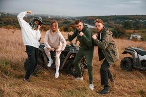 Two couples is with quad bikes on the field. Men are having fun and showing the, fists photo