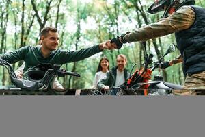 Knocking fists, gesture. Two couples on ATV with man that is on the bike in the forest. photo