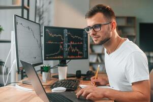 Laptop is on the table. Young, stock broker is working in the office by using computer photo