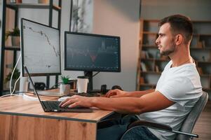 Laptop is on, the table. Young stock broker is working in the office by using computer photo