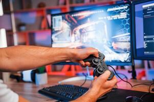Close up view of hands with, joystick controller. Male game streamer in casual clothes is indoors with pc photo