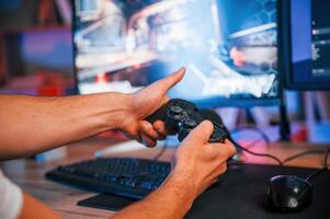 Close up view of hands with joystick controller.. Male game streamer in casual clothes is indoors with pc photo