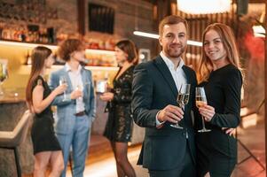 Man with, his woman ,is standing and smiling. Group of people in beautiful elegant clothes are celebrating New Year indoors together photo