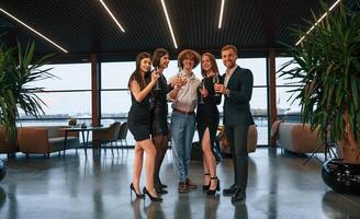 Smiling, for the camera. Group of people in beautiful elegant clothes are celebrating New Year indoors together photo