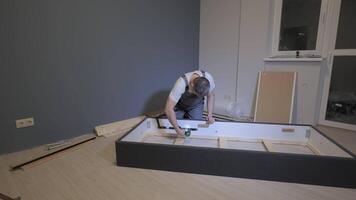 Timelapse of A builder in a work overalls is assembling a bed. Assembling furniture in a new apartment. video
