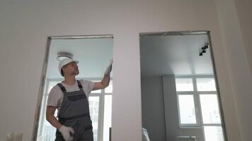 A builder in working uniform checks the size and quality of doorways in a new apartment. The concept of construction and repair. Bottom view, 4K video