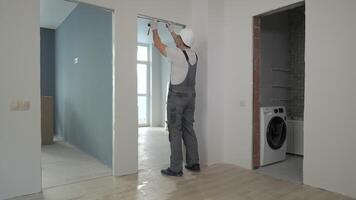 A builder in working uniform checks the size and quality of doorways in a new apartment. The concept of construction and repair. video
