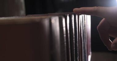 A mans hand is looking for the right book among a collection of volumes of books on a wooden bookshelf. Close Up. Shallow depth of field. Ultra 4K video