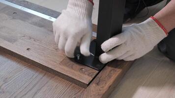 Builder in overalls screwing table legs using a screwdriver. Assembling furniture in a new apartment. video