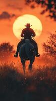 Cowboy riding horse at sunset in open field with vibrant orange sky and silhouettes of trees photo