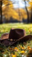 Brown cowboy hat resting on vibrant autumn grass surrounded by colorful leaves in a serene outdoor setting photo