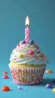 Colorful birthday cupcake with a lit candle and decorative sprinkles on a blue background photo