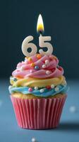 Festive cupcake with colorful frosting and a lit candle celebrating a 65th birthday photo