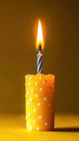 Bright yellow candle with a lit birthday candle on top against a yellow background photo