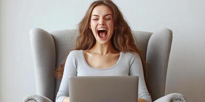 Young woman expresses excitement while using a laptop in a cozy living room setting during daytime photo