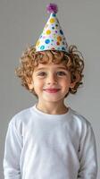 Young child wearing a party hat smiles joyfully in a simple indoor setting during a birthday celebration photo
