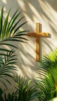 Wooden cross on a textured wall surrounded by green palm plants in soft sunlight photo