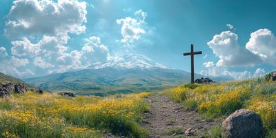 Cross on a hillside with flowers and a mountain backdrop under blue sky and clouds at midday photo