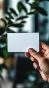 Hand holding a blank card in front of a leafy background in a modern indoor setting photo