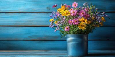 Colorful wildflowers in a blue tin vase against a wooden backdrop bring joy to any setting photo
