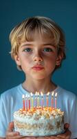 Boy celebrates birthday holding cake with lit candles, surrounded by festive atmosphere in a simple interior setting photo