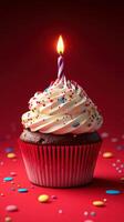 Delightful birthday cupcake with a lit candle and colorful sprinkles against a vibrant red background photo