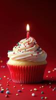 Colorful cupcake with a candle and sprinkles on a vibrant red background during a celebration photo