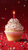 Delicious cupcake with white frosting and a candle surrounded by colorful sprinkles on a festive red background photo