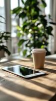 Casual workspace setup with a tablet and coffee cup surrounded by natural light and greenery photo