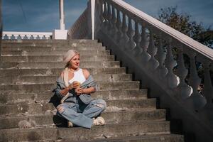 A woman sits on a set of stairs, holding a cup of coffee. She is enjoying her coffee and taking in the view from the top of the stairs. photo