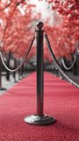 Elegant red carpet lined with stanchions under vibrant red trees in soft lighting creating a luxurious atmosphere photo