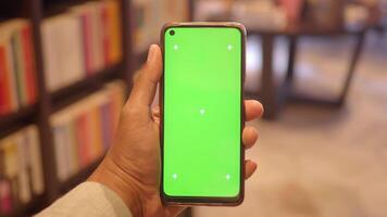 Hand holds smartphone displaying a green screen in a library video