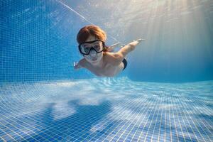 Small boy in mask swimming underwater of pool photo
