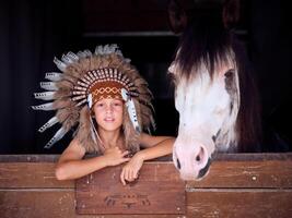 Kid in Native American costume standing with horse in stable photo