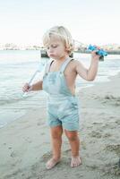 Serious curious toddler playing with soap bubble toy on beach in photo