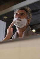 Happy male applying shaving foam in bathroom photo