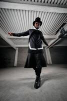 Stylish ethnic man in round sunglasses and hat standing in under photo
