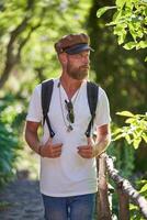 Traveling bearded man in cap walking in forest photo