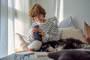 Smiling schoolboy with aged photo camera and dog on bed