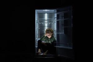 Focused kid watching movie on tablet while sitting in fridge photo