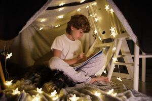 Focused boy drawing in blanket fort at home photo