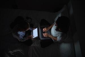 Mother with son browsing gadgets while doing homework in darknes photo