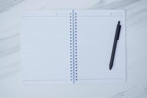 An open notebook and a black pen are displayed on a surface photo