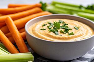 Creamy carrot dip garnished with parsley with fresh vegetables surrounding it photo